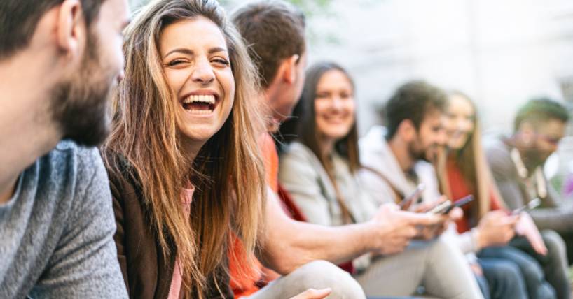 Group of trendy young people chatting together sitting on a bench outdoors